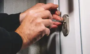 Ręce z wytrychem próbują otworzyć zatrzaśnięte drzwi.