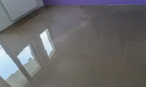Lśniąca posadzka z anhydrytu, odbijająca światło okien i fioletową ścianę.