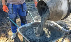 Robotnik w pomarańczowych rękawicach wylewa beton B25 z betoniarki do taczki. Cena za m3 jest atrakcyjna.