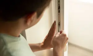 Mężczyzna dokonuje regulacji drzwi balkonowych uchylnych, dokręcając śrubę śrubokrętem.