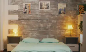 Przytulna sypialnia bez okna, z łóżkiem w turkusowej pościeli i drewnianą ścianą. Lampki nocne tworzą ciepły nastrój.