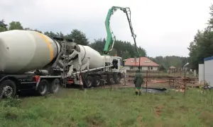 Betoniarka z pompą przygotowuje jaki beton na strop. Na placu budowy widać dom w tle i pracownika w zielonej kurtce.