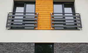 Nowoczesny portfenetr z drewnianym akcentem i ciemną balustradą. Poniżej kamienna okładzina.