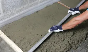 Ręce w rękawiczkach wygładzają świeży styrobeton za pomocą łaty.