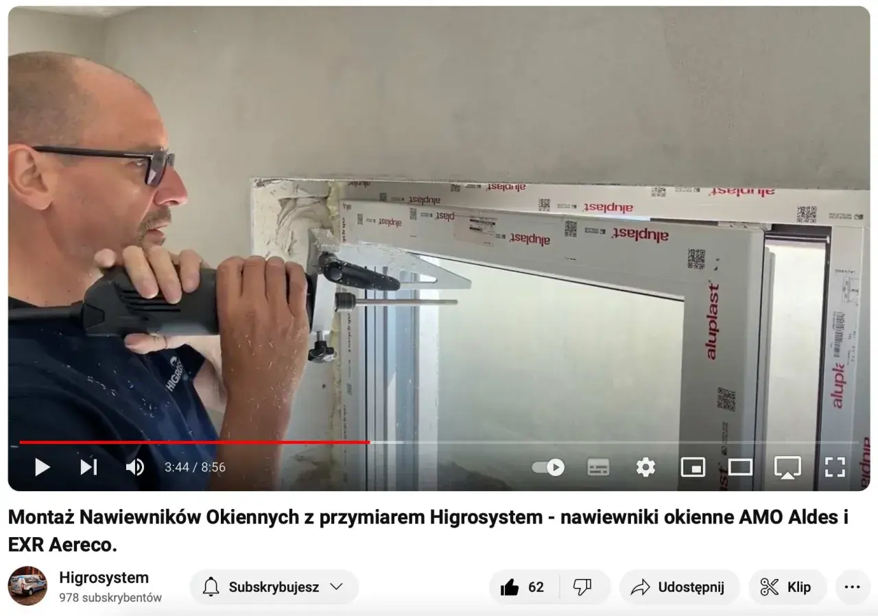 Montaż nawiewników okiennych z przyrządem Higrosystem. Widać mężczyznę wiercącego otwory w ramie okiennej, przygotowując miejsce na wywietrzniki w oknach.
