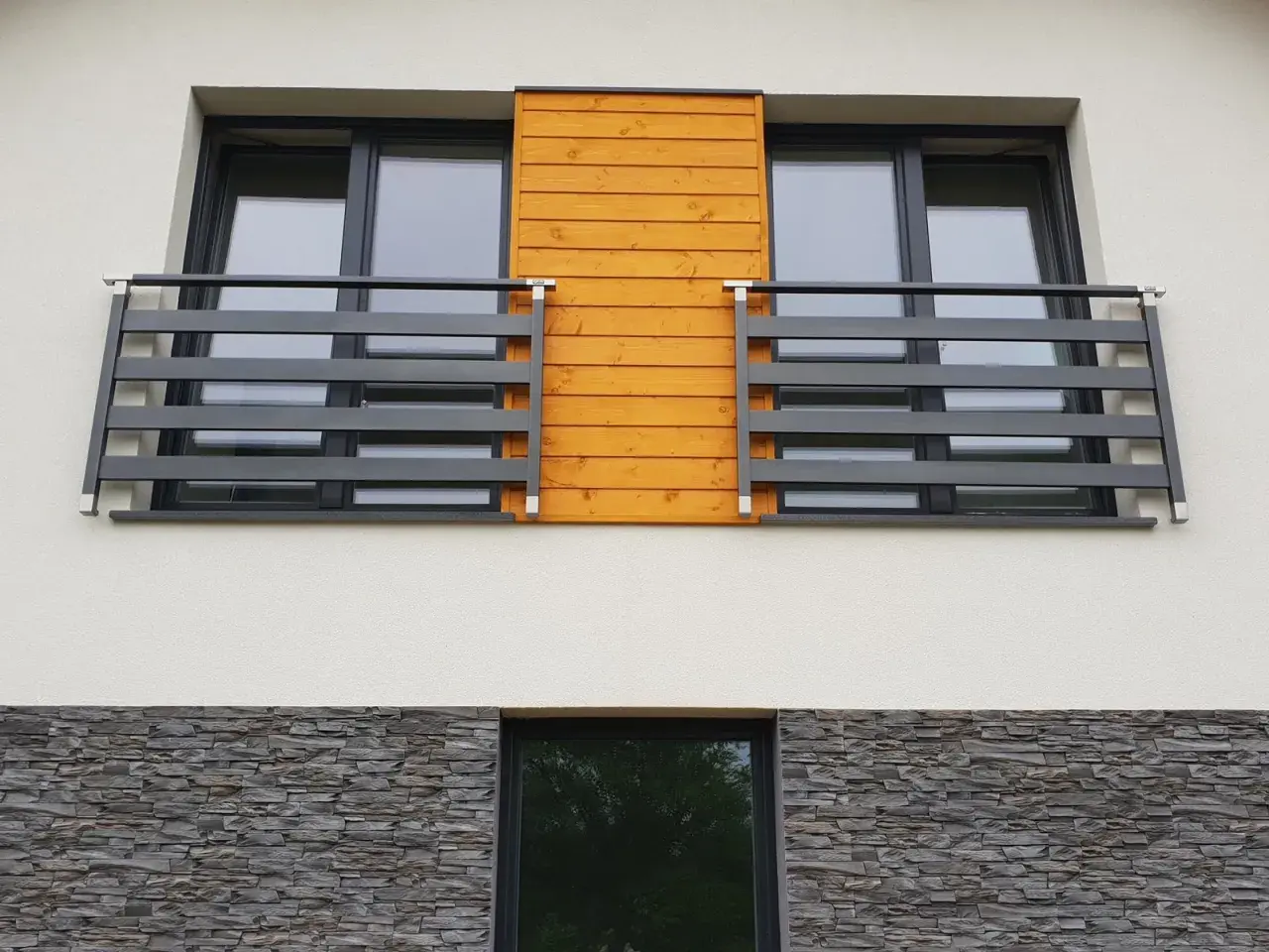 Nowoczesny portfenetr z drewnianym akcentem i ciemną balustradą. Poniżej kamienna okładzina.