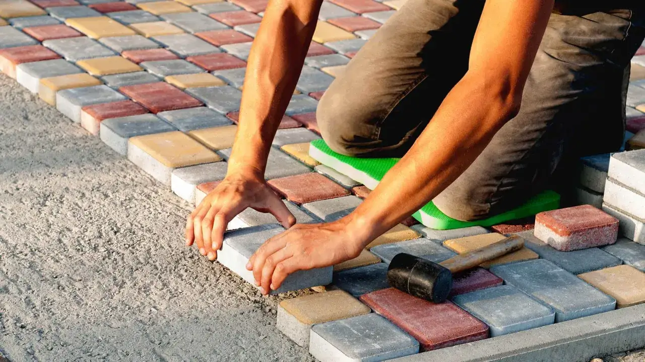 Układanie kolorowej kostki brukowej na podsypce z półsuchego betonu. Dłonie pracownika precyzyjnie dopasowują kolejny element.