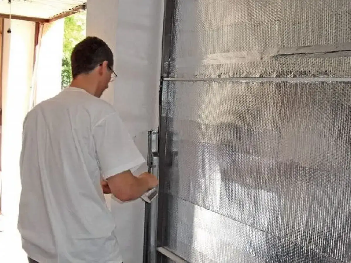 Mężczyzna montuje materiał izolacyjny, wykonując ocieplenie bramy garażowej.