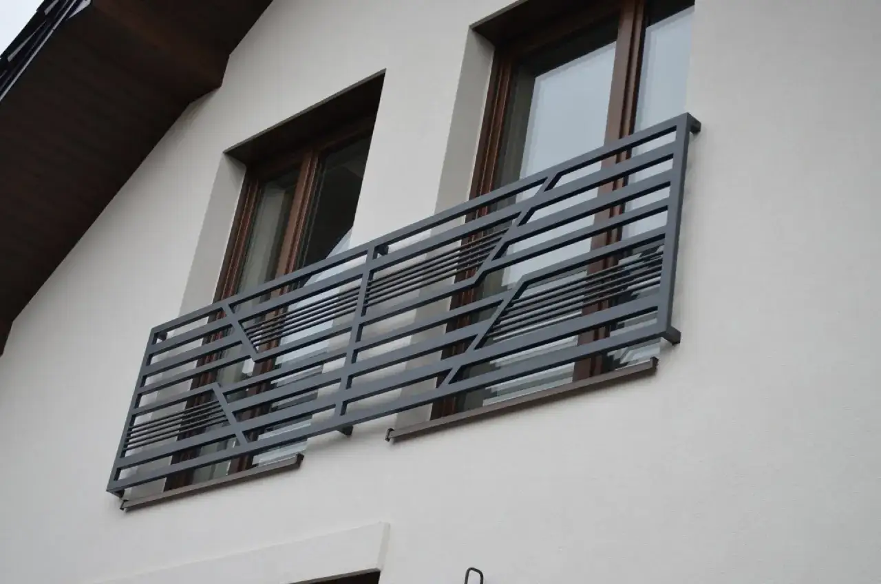 Nowoczesny portfenetr z metalową, geometryczną balustradą przed dwoma oknami.