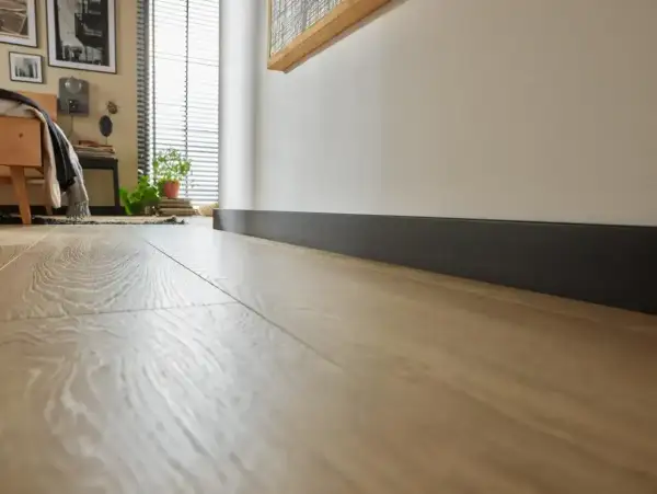 Nowoczesne, ciemne cokoły podkreślają jasną podłogę w sypialni.