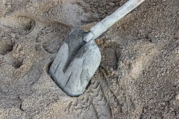 Łopata zagłębiona w piasku, gotowa do pracy. Waga 1m3 betonu suchego to ok. 1600 kg.