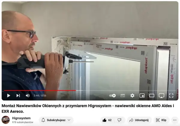 Montaż nawiewników okiennych z przyrządem Higrosystem. Widać mężczyznę wiercącego otwory w ramie okiennej, przygotowując miejsce na wywietrzniki w oknach.