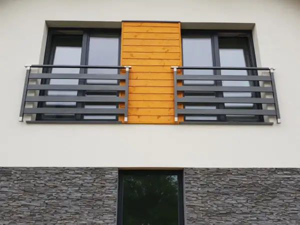 Nowoczesny portfenetr z drewnianym akcentem i ciemną balustradą. Poniżej kamienna okładzina.