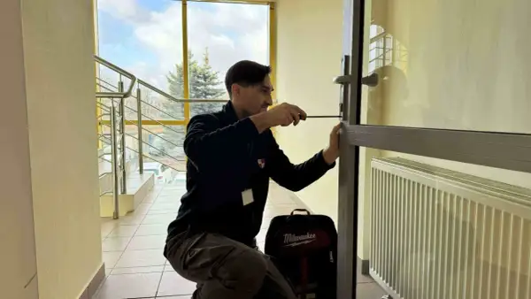 Mężczyzna próbuje otworzyć drzwi bez klucza, używając śrubokręta. Obok niego stoi torba z narzędziami.