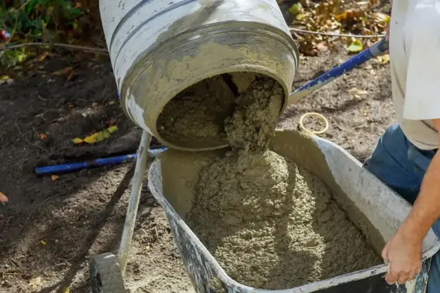 Świeża porcja betonu z betoniarki trafia do taczki, gotowa do budowy fundamentów.